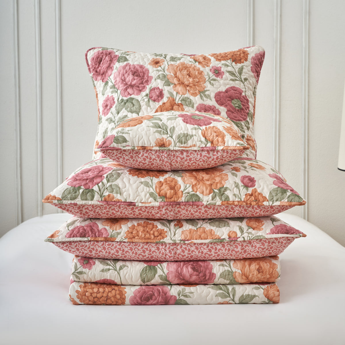 Terracotta floral quilt bedding layered with coordinating decorative accent pillows and shams
