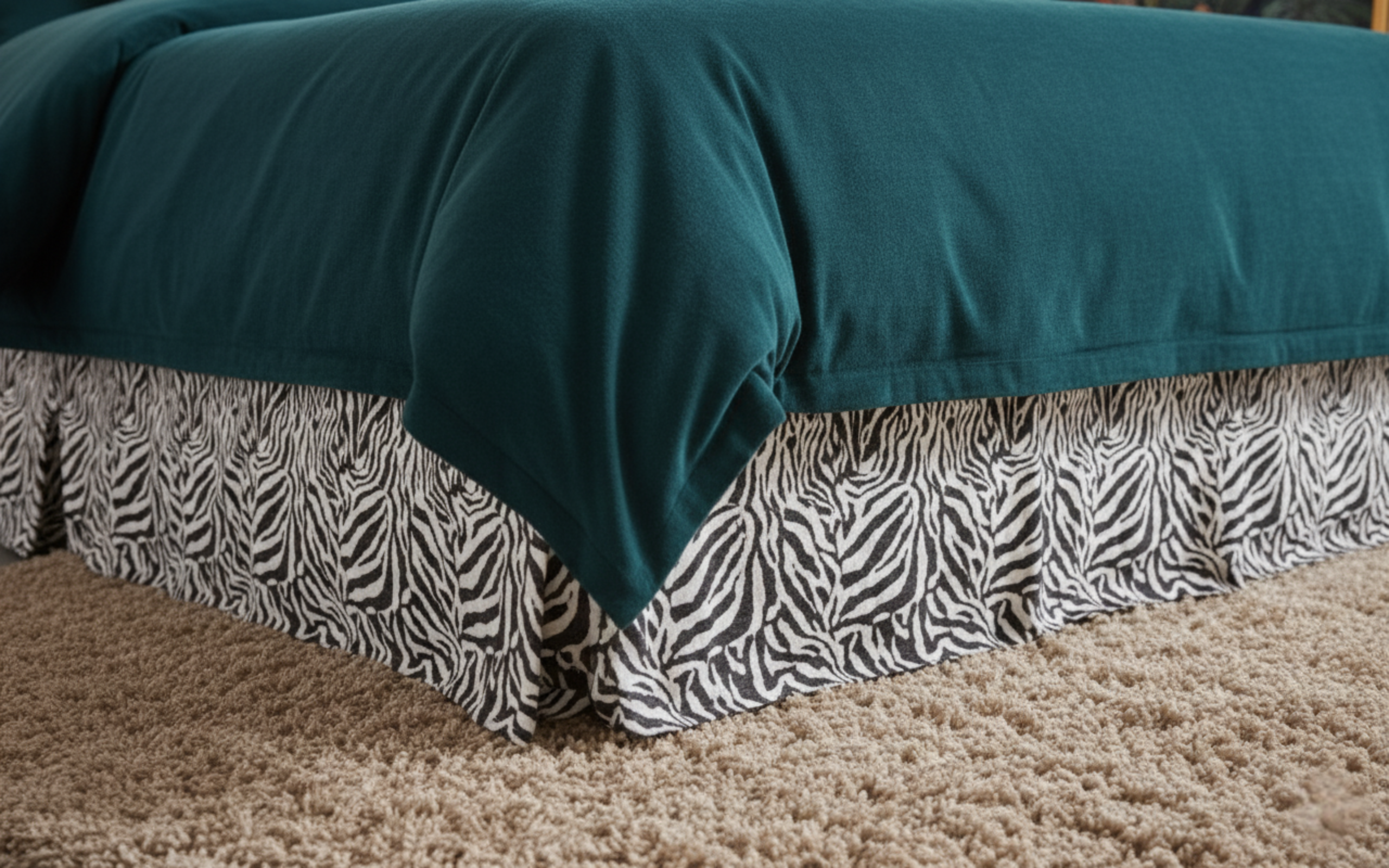 Teal comforter with zebra patterned bed skirt on a bed.