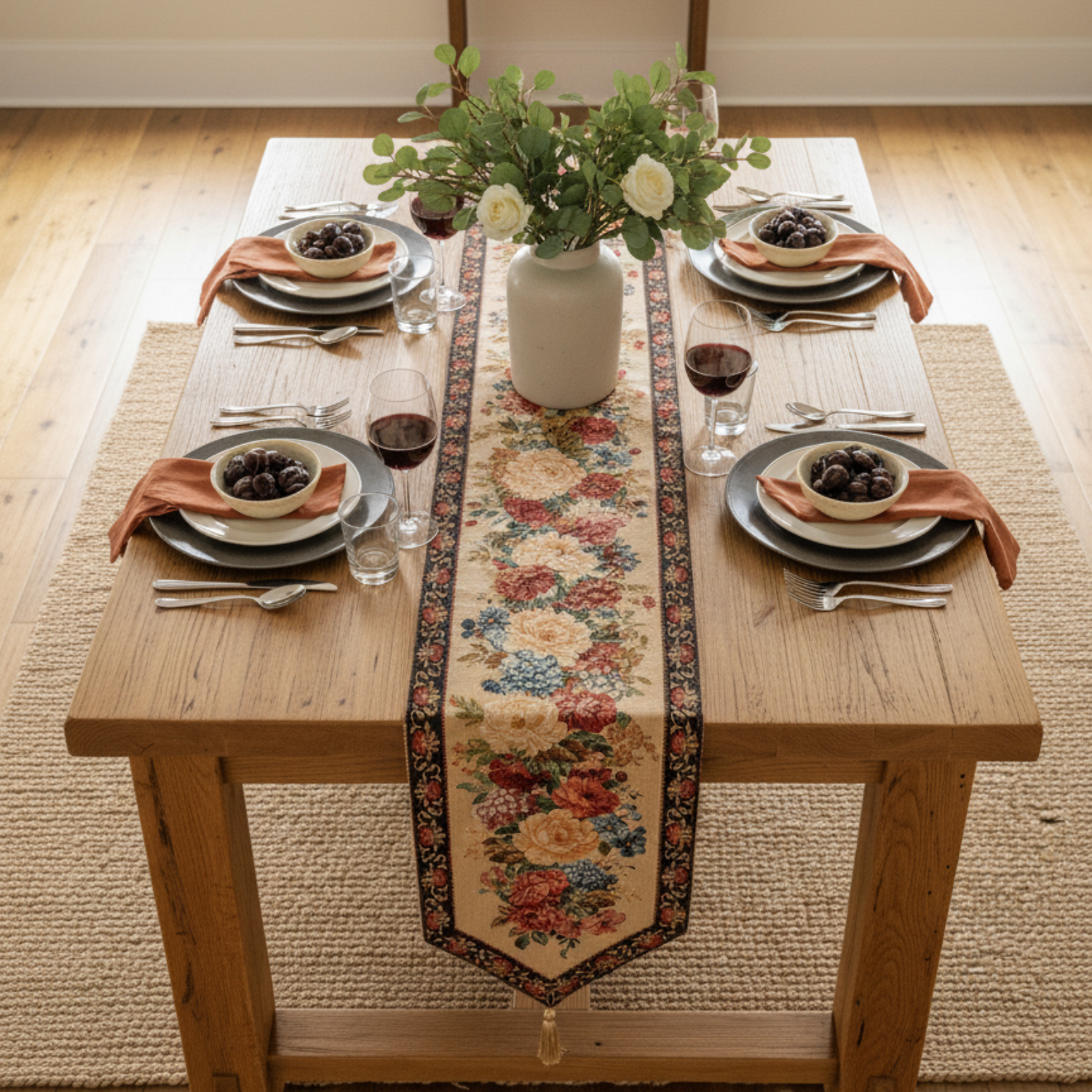 Dining table set with floral table runner, plates, glasses, and flowers.