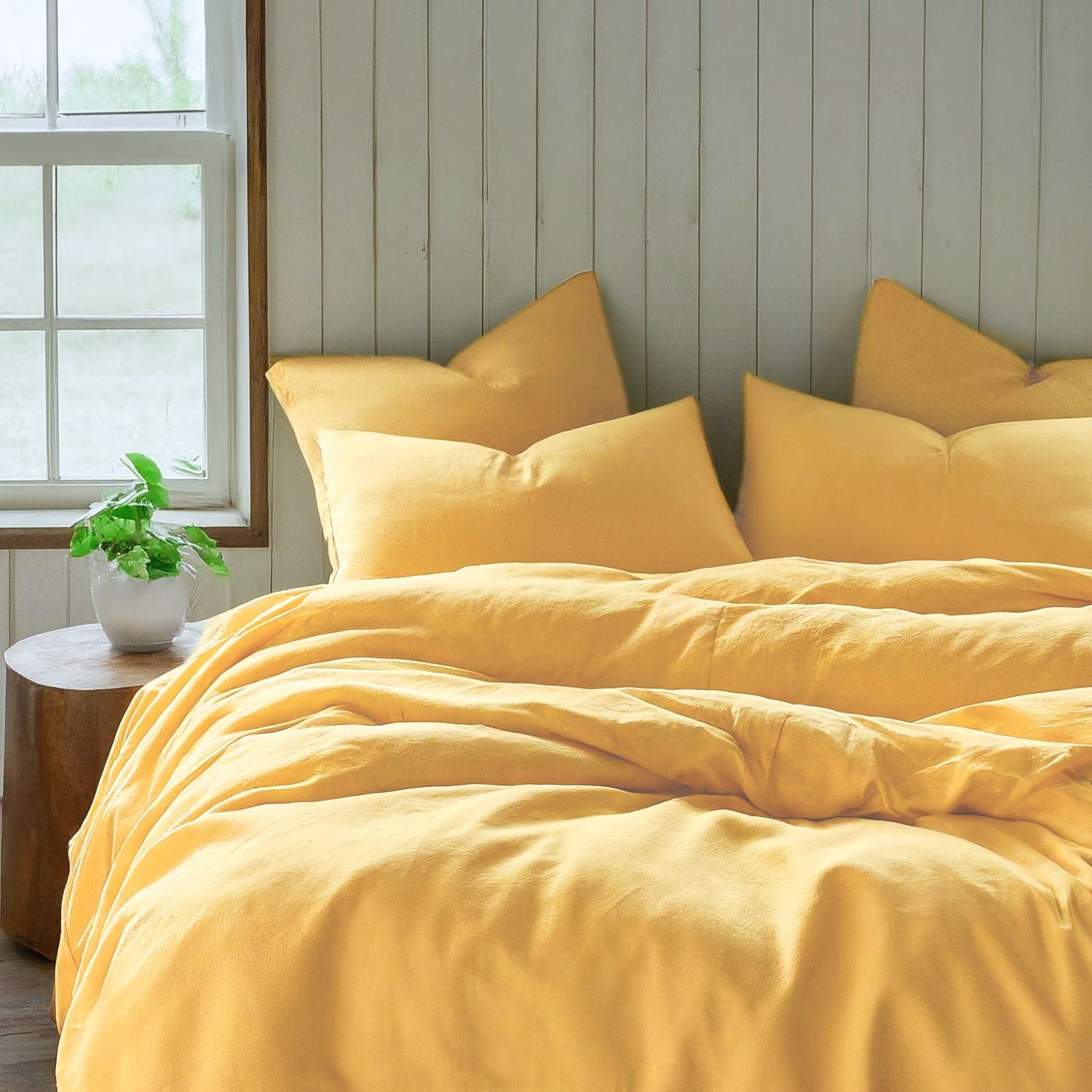 A bed with a soft light yellow duvet cover and  pillows next to a window in a farmhouse Bedroom