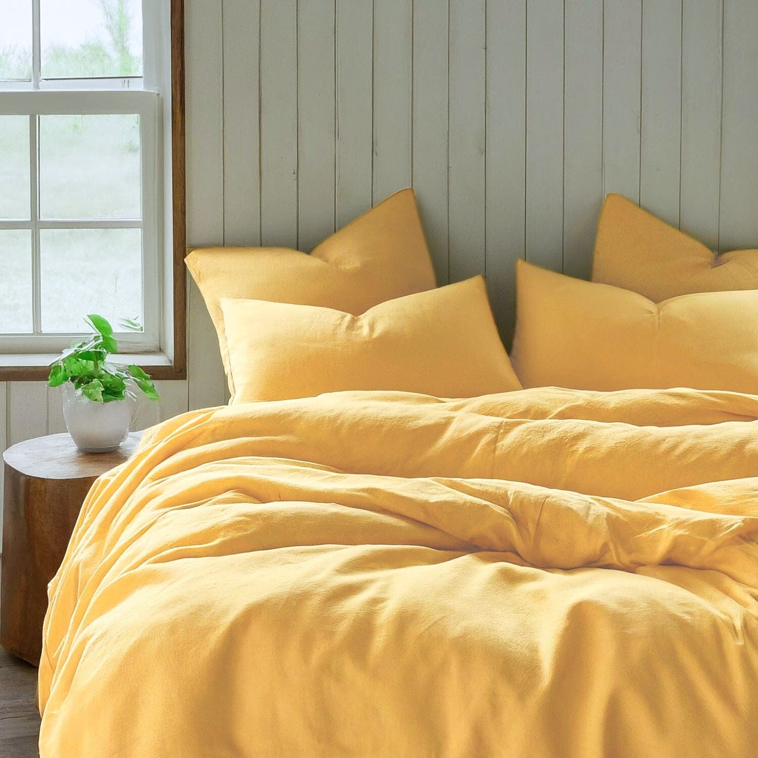 A bed with a soft light yellow duvet cover and pillows next to a window in a farmhouse Bedroom