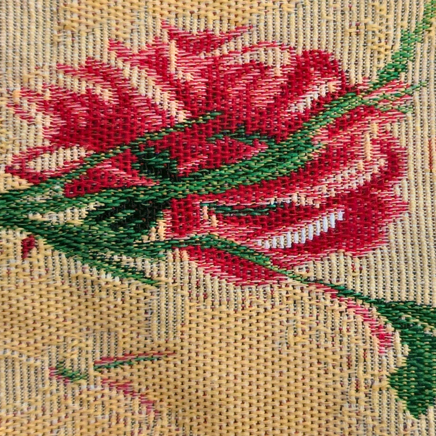Close-up of a needlepoint or embroidery piece with red flowers and green leaves on a beige background.