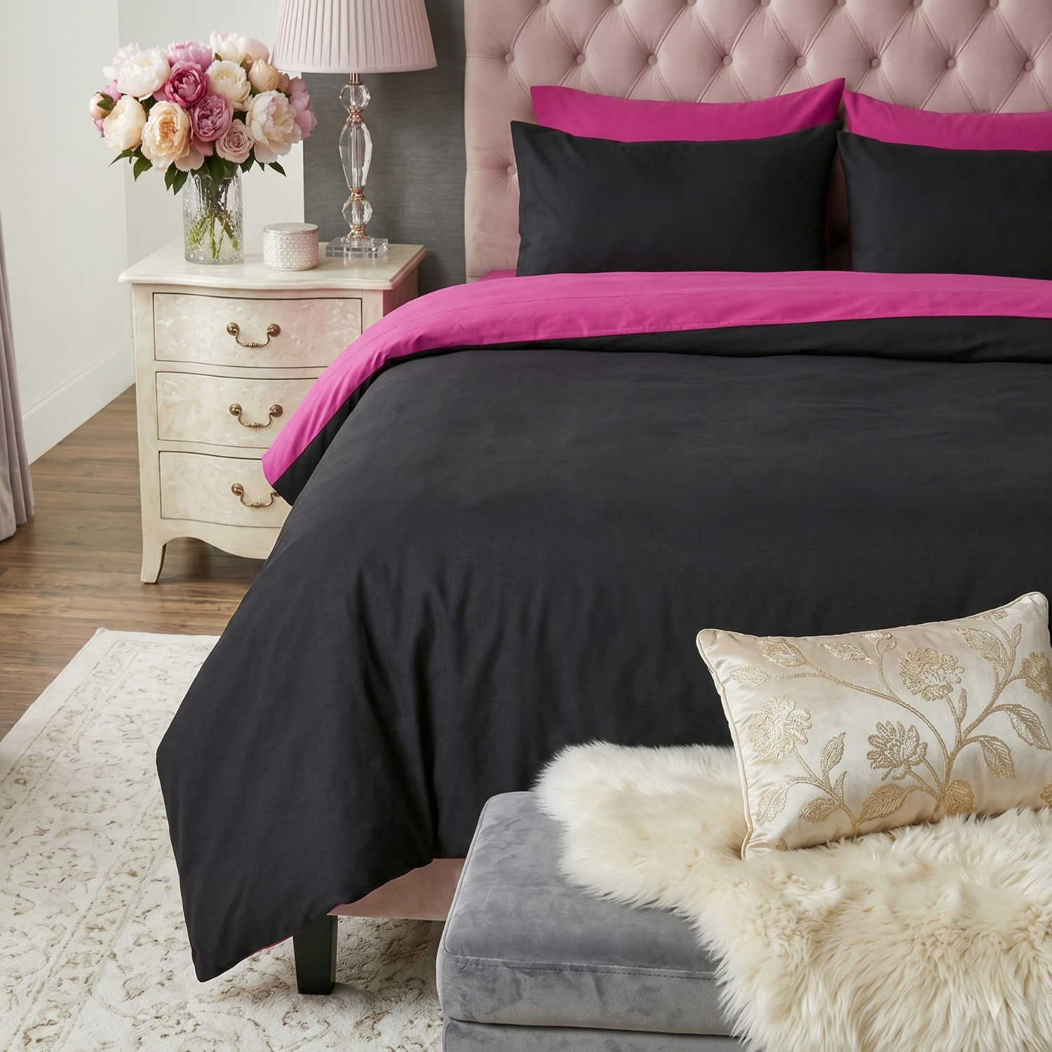 A modern bedroom featuring the Tache cotton hot pink and black reversible comforter set. The bed is styled with a pink tufted headboard, the black comforter folded back to reveal hot pink sheets, and matching pillowcases