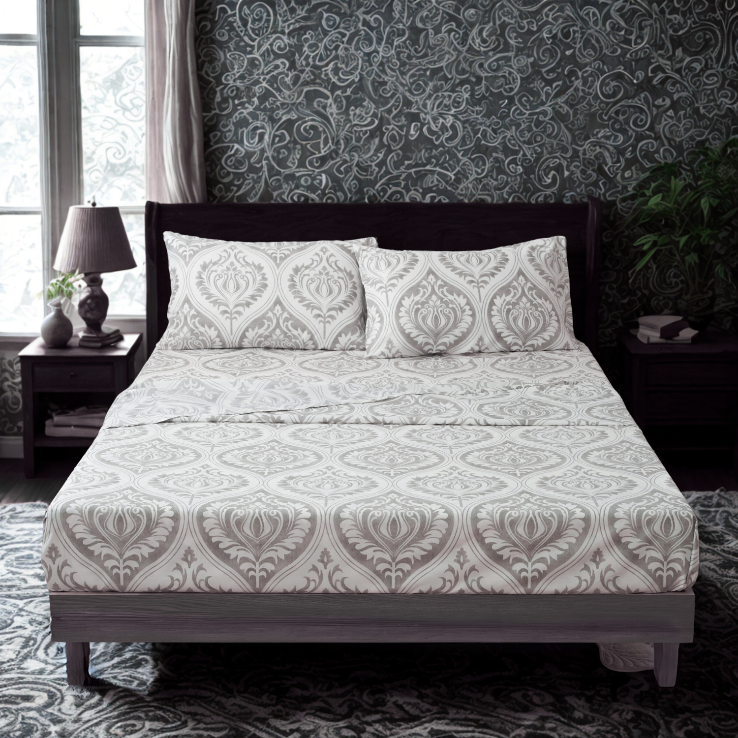 A modern bedroom features a bed with a white bed sheet set adorned with an intricate gray floral paisley pattern. The bed is flanked by two dark wooden nightstands, one with a lamp and small vase, and the other with a stack of books. The room has a dark, ornate wallpaper with swirling patterns, a large window with sheer curtains, and a patterned rug on the floor. A green plant adds a touch of nature to the corner