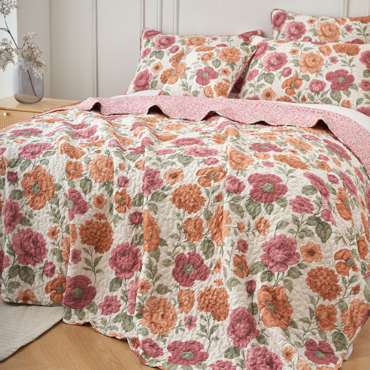 Close up of terracotta roses, dusty pink blooms and sage green leaves on the ivory quilted bedspread