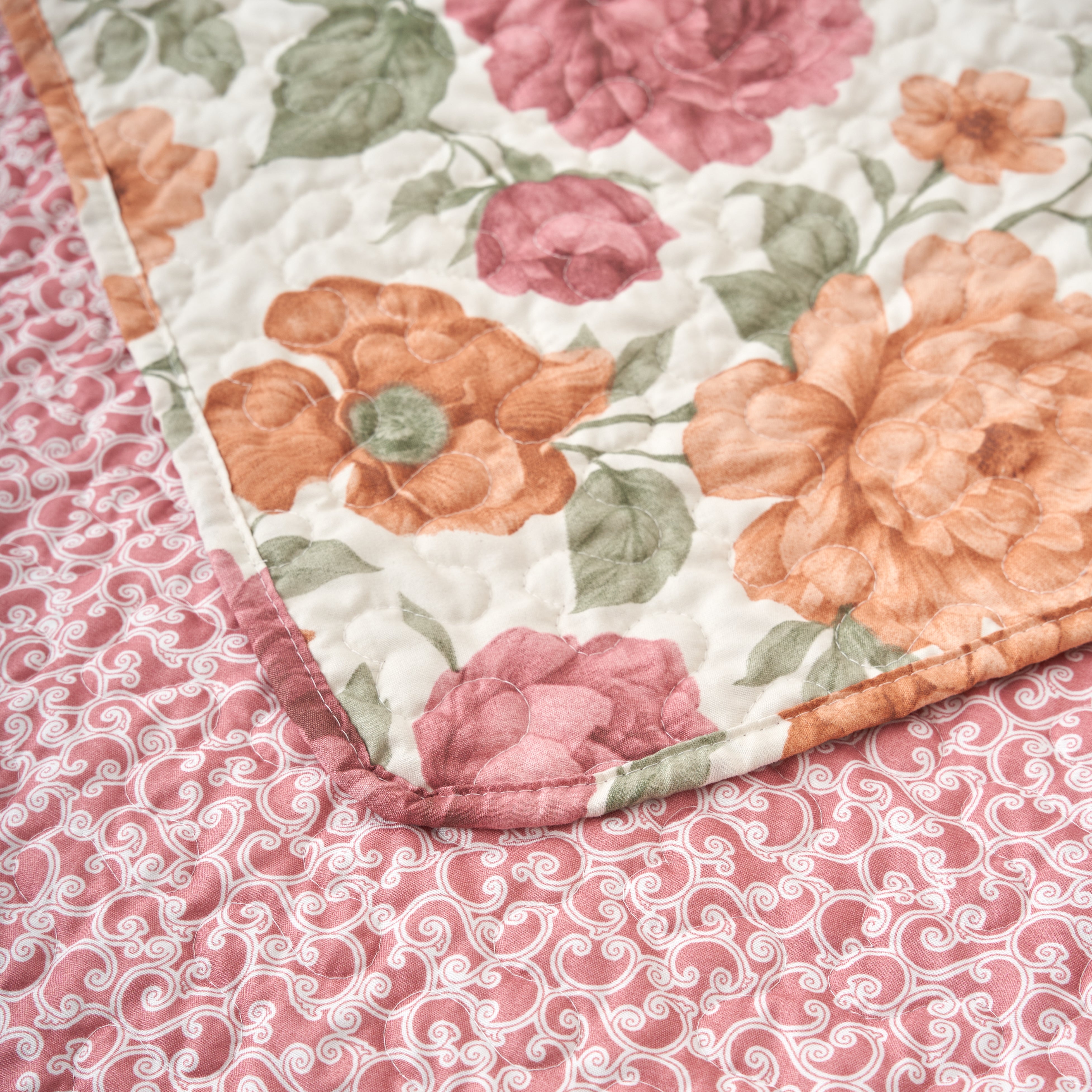 Folded corner of the terracotta rose floral quilt showing the reversible ivory scroll underside