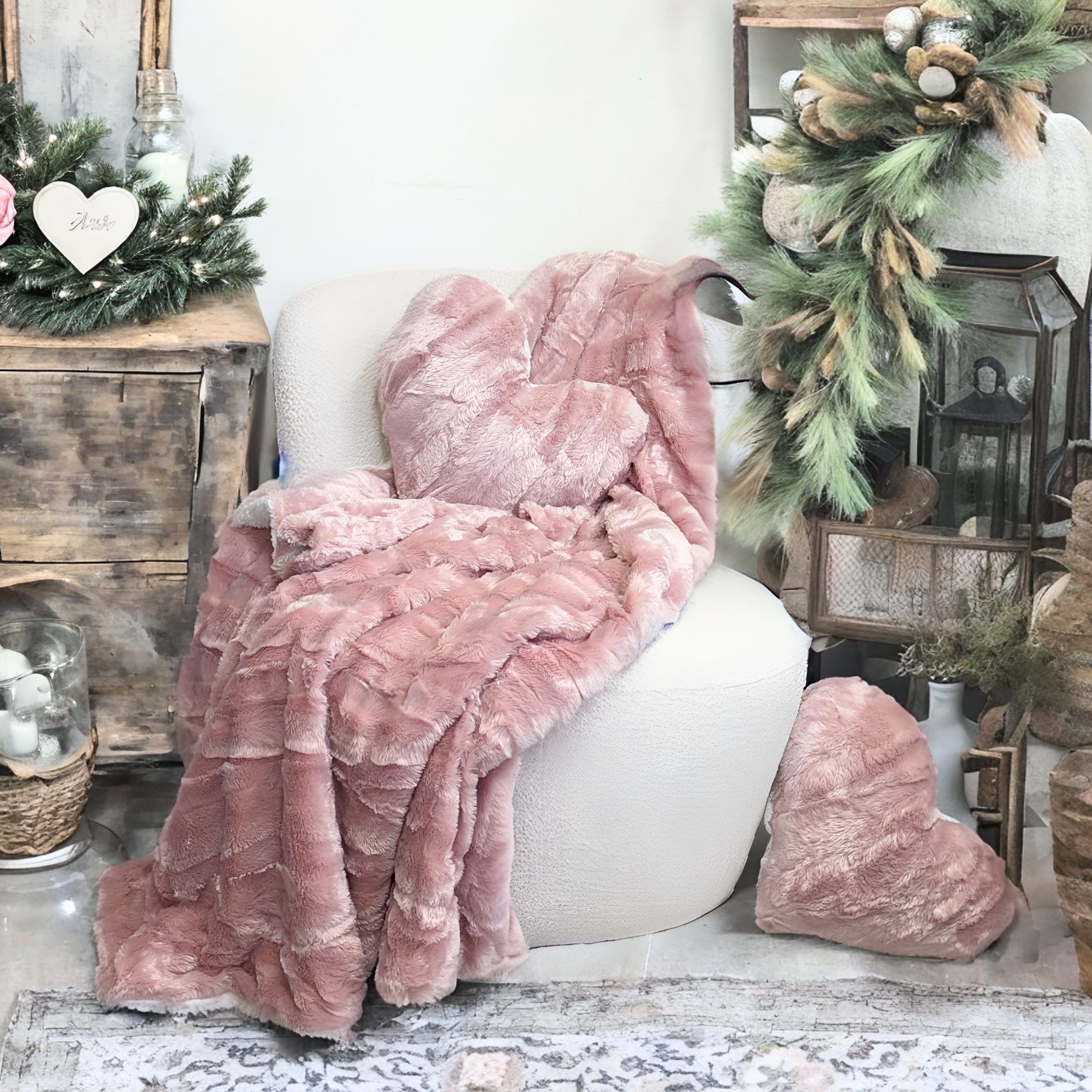 A cozy faux fur blush dusty rose pink plush blanket and a heart-shaped pillow rest on a white armchair