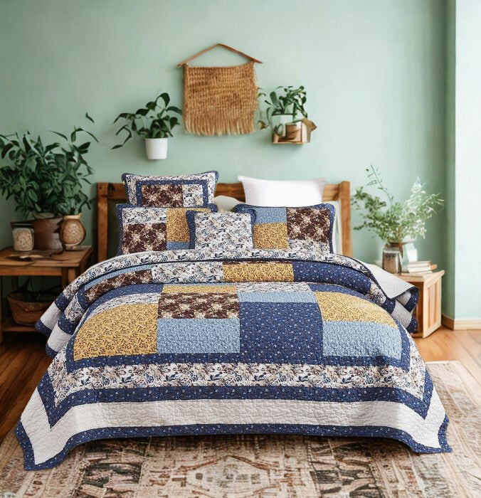 A cozy bedroom features a bed with a patchwork quilt in blue, yellow, and white with intricate floral patterns. The bed is flanked by two wooden nightstands, one with potted plants and small items, and the other with books. The room has teal walls adorned with a woven wall hanging and a shelf with plants, a large window with sheer curtains, and a patterned rug on the wooden floor, with additional greenery enhancing the space