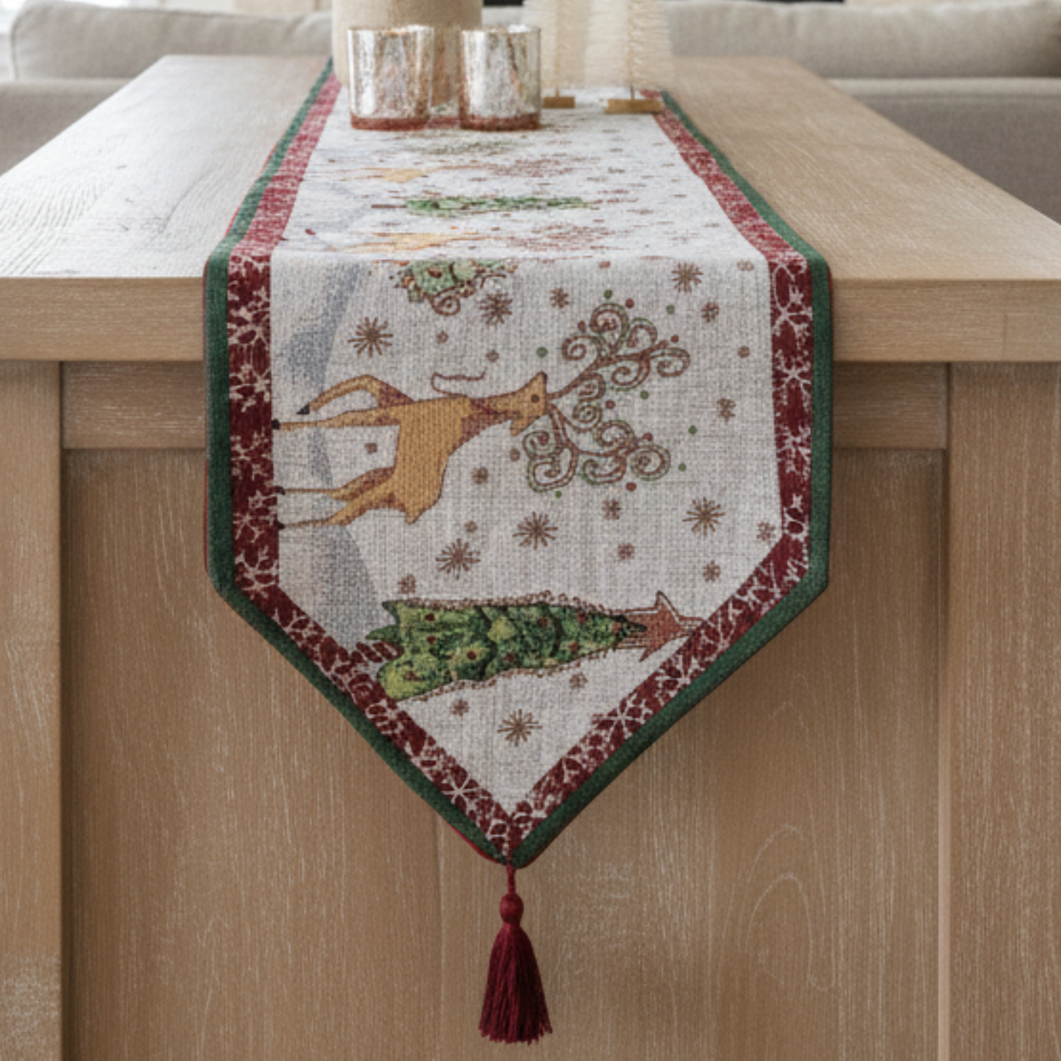 Decorative festive tapestry table runner with reindeer and Christmas tree design on a wooden surface.