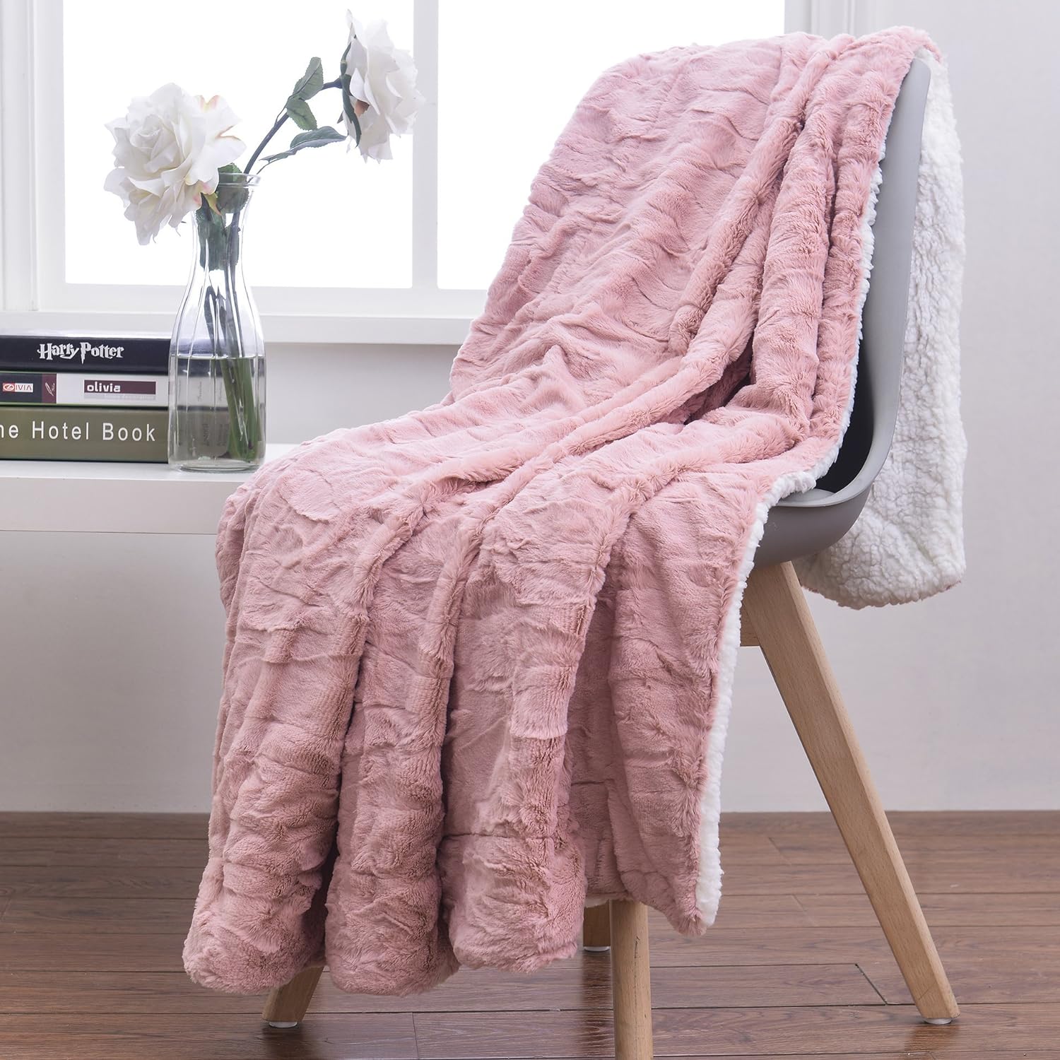 A cozy faux fur blanket in rose pink is draped over a chair next to a vase of fresh flowers
