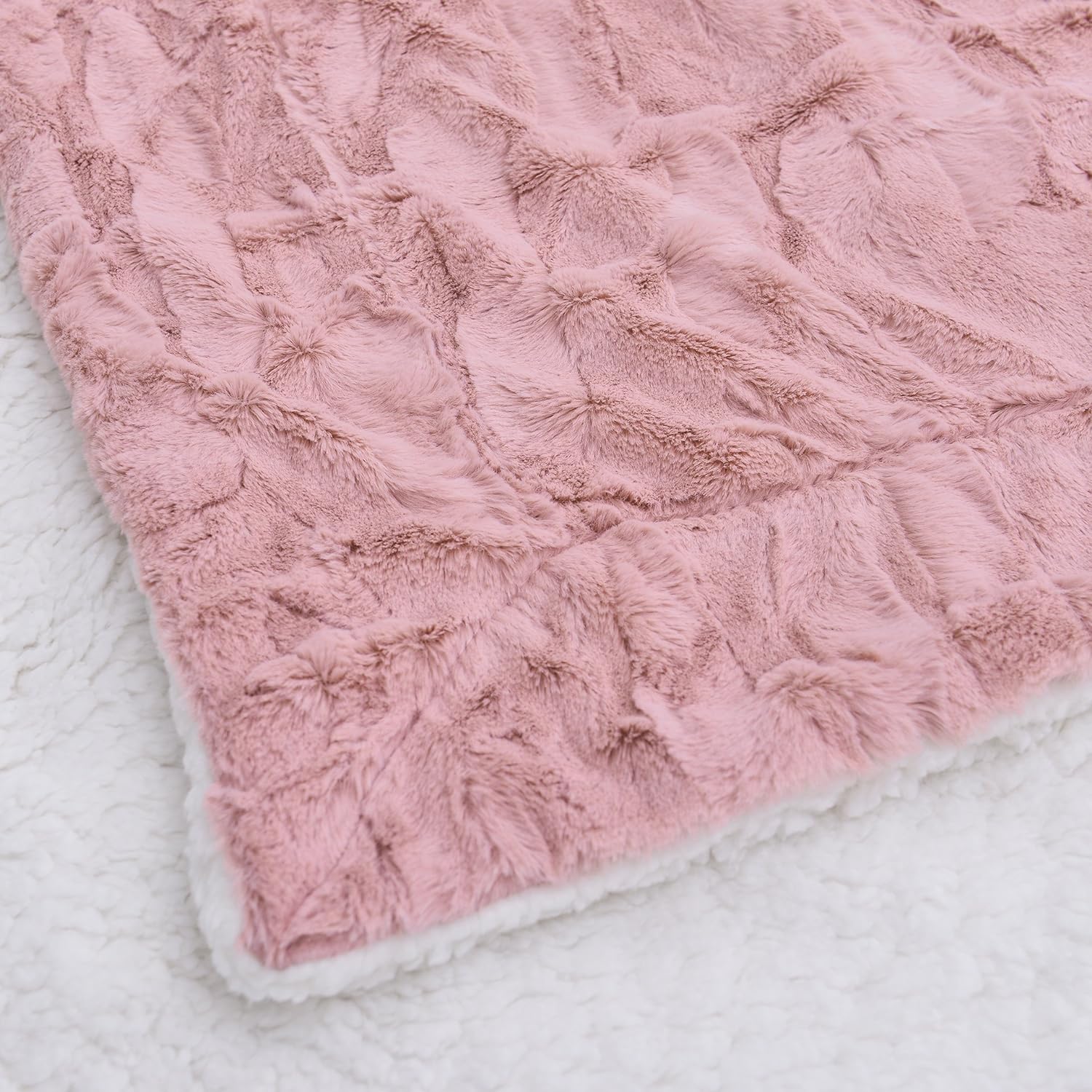 A close-up view of a soft pink blanket with a slightly darker pink satin border. The blanket is wrinkled and appears to be lying on a bed.