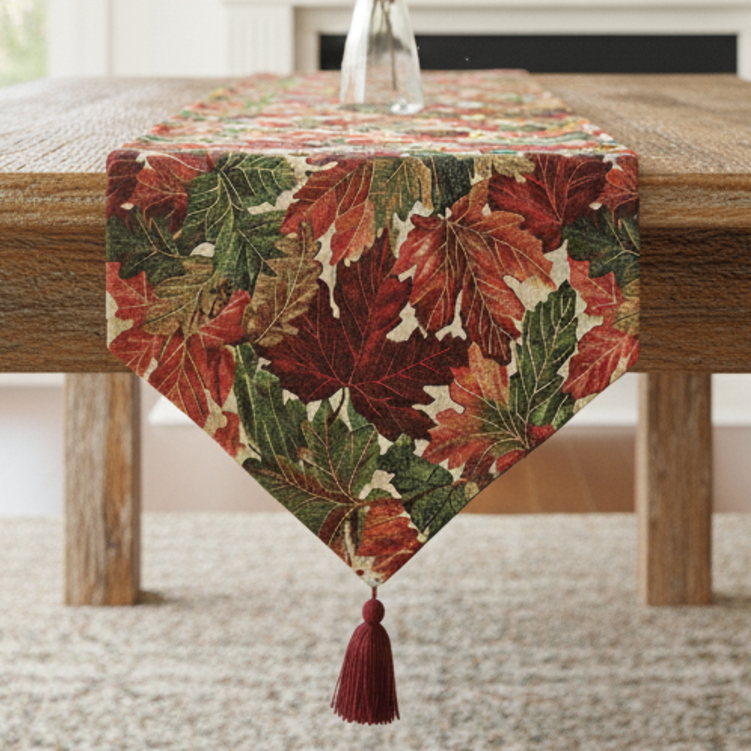 Autumn-themed table runner with leaves and a tassel on a wooden table.
