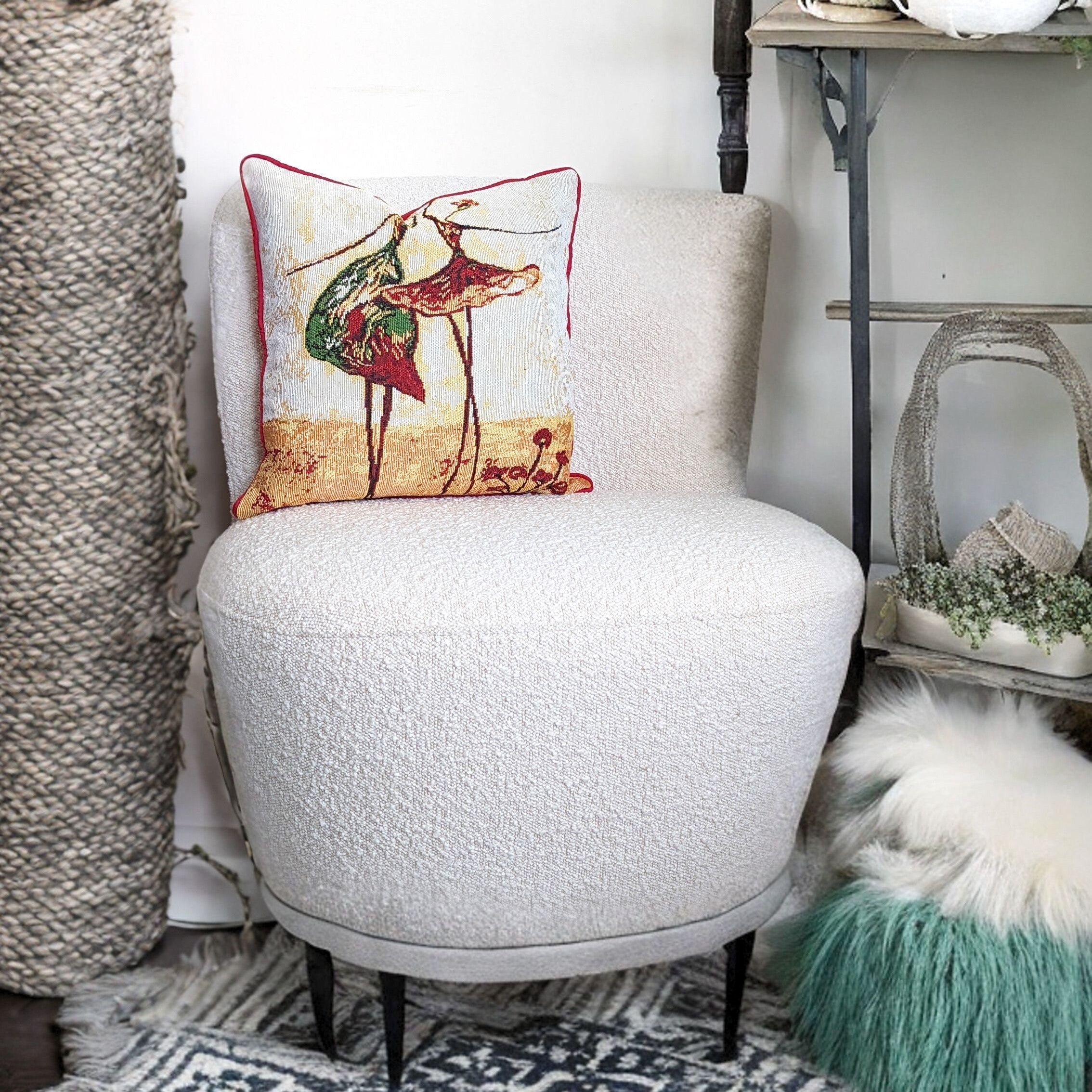 A white chair with a pillow on it in a living room. The Tapestry Throw has an abstract art picture of two dancing ladies. 