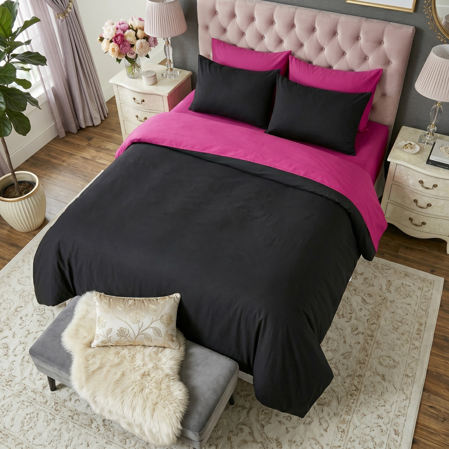 Tache 6-piece cotton hot pink and black reversible comforter set displayed on a bed with a pink tufted headboard. The modern glam room includes a white nightstand with flowers and a grey footboard bench with a white faux fur throw.
