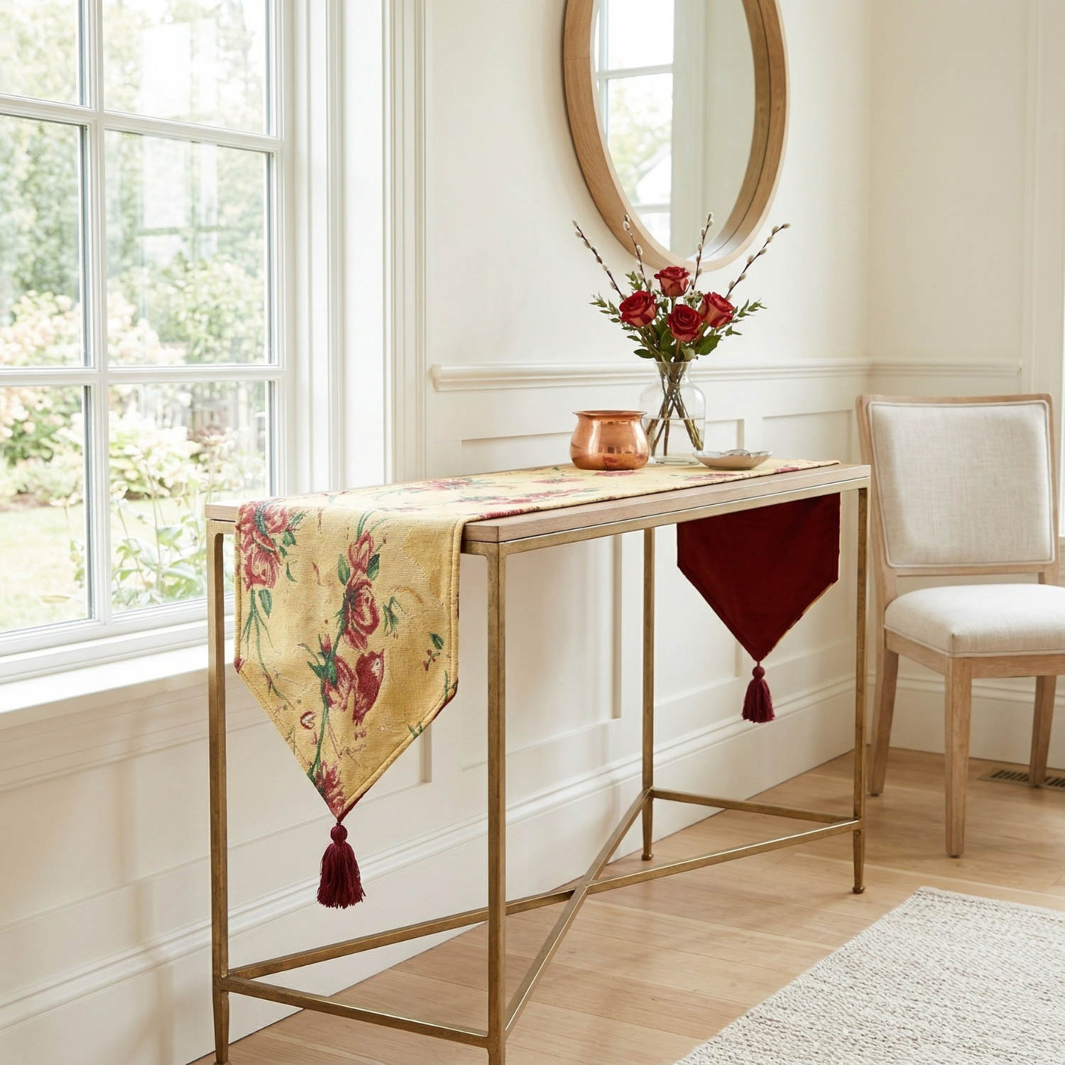Tache golden woven tapestry table runner featuring red roses, birds, and a red tassel, draped over a console table next to a vase of red flowers.
