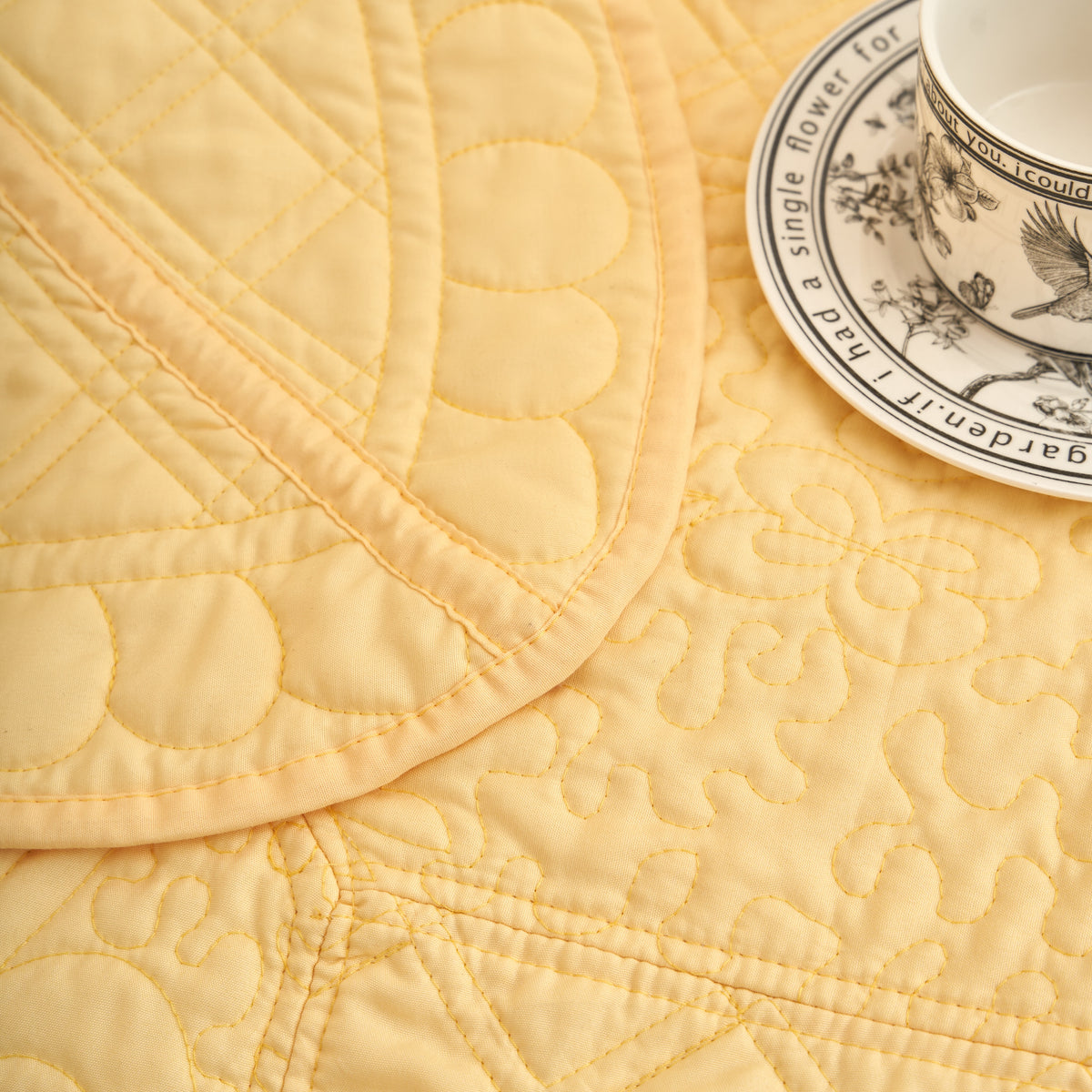 Embossed floral medallion quilting along the scalloped border of a buttercup yellow throw