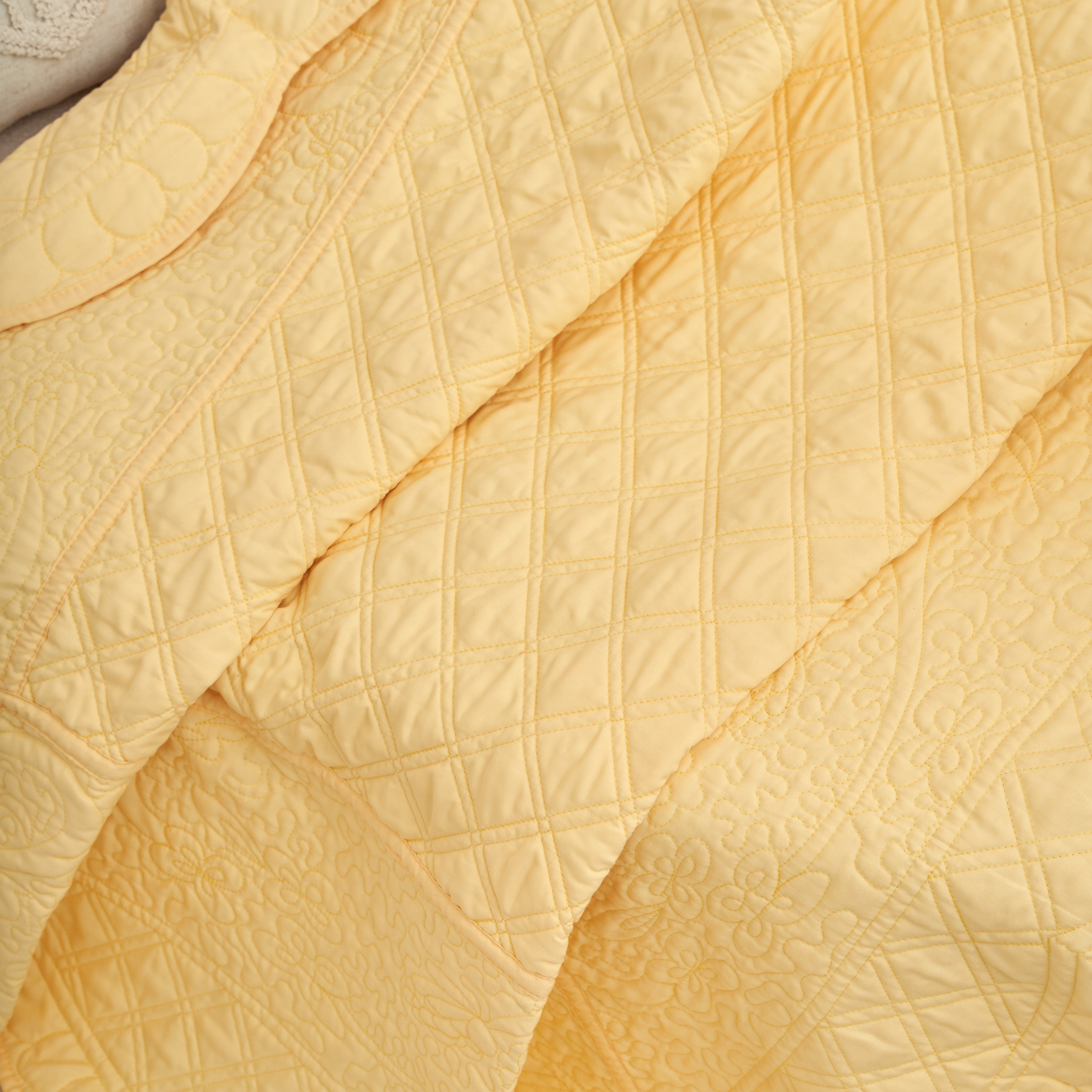 Diamond and floral matelasse stitching detail on a buttercup yellow quilted throw blanket